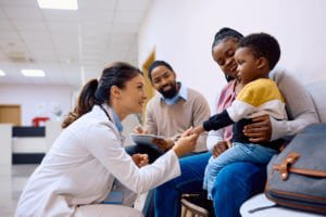 A female pediatrician is talking to a little boy sitting on his mother's lap at the Family Medicine clinic.
