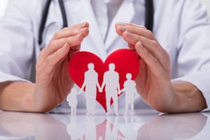 Image of a doctor protecting a family, cut out in a heart shape to illustrate family medicine for preventive care.
