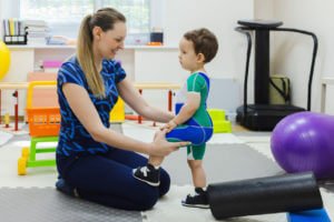 Physiotherapist assisting a little child during pediatric physical exam.