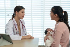 Female pediatrician doctor and young mother discuss baby's health during pediatric appointment.