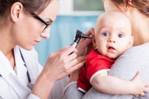 Doctor examining baby boy with otoscope during pediatric physicals.