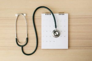 Stethoscope with calendar page date on wood table representing annual physical exam.