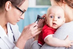 A doctor uses an otoscope to examine a baby boy's ear during a pediatric physical at Abundance Health Care