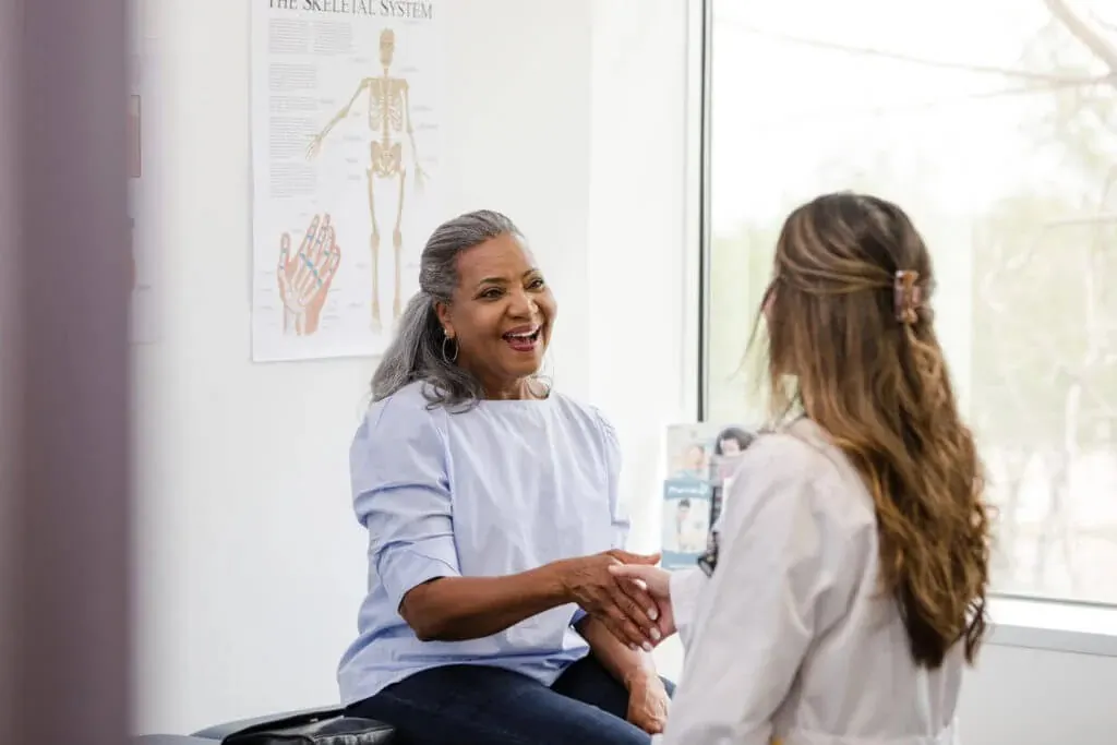 An elderly woman smiles and shakes hands with her doctor during a checkup visit