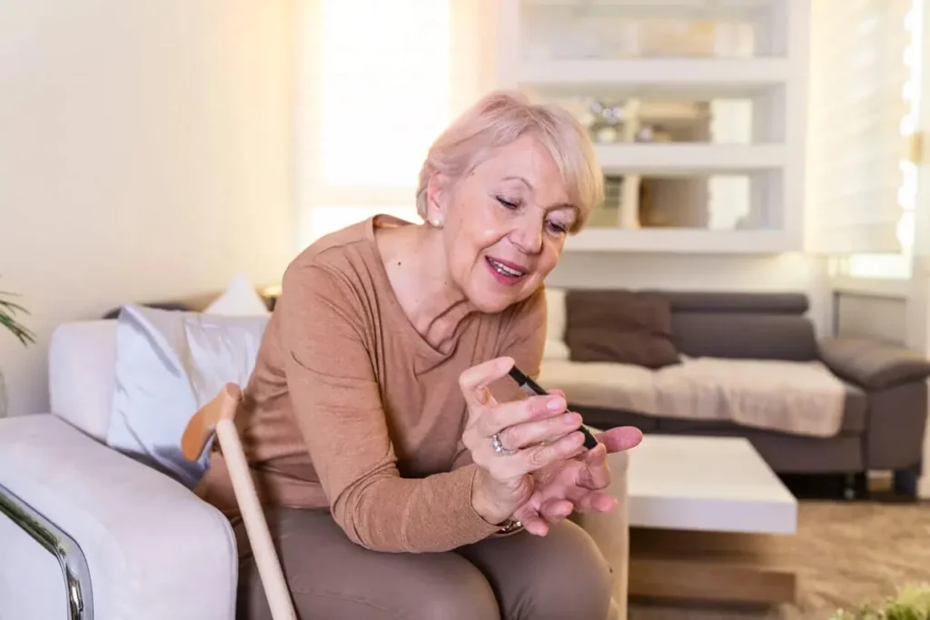 An elderly woman smiles while checking her blood glucose level at home using a fingertip test
