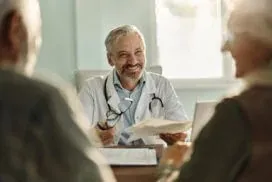 A smiling family medicine provider reviews paperwork with an older adult couple during a visit at Abundance Health Care