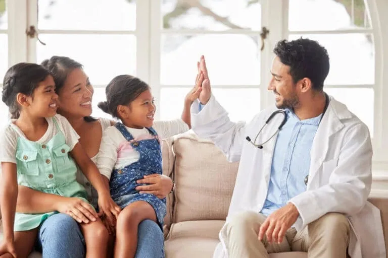 A smiling girl high-fives her family medicine provider at Abundance Health Care after receiving positive test results