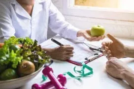A provider hands a patient an apple while reviewing a weight management and nutrition plan