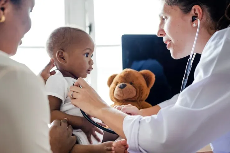 Pediatrician using a stethoscope to check an infant during a wellness visit with a parent present