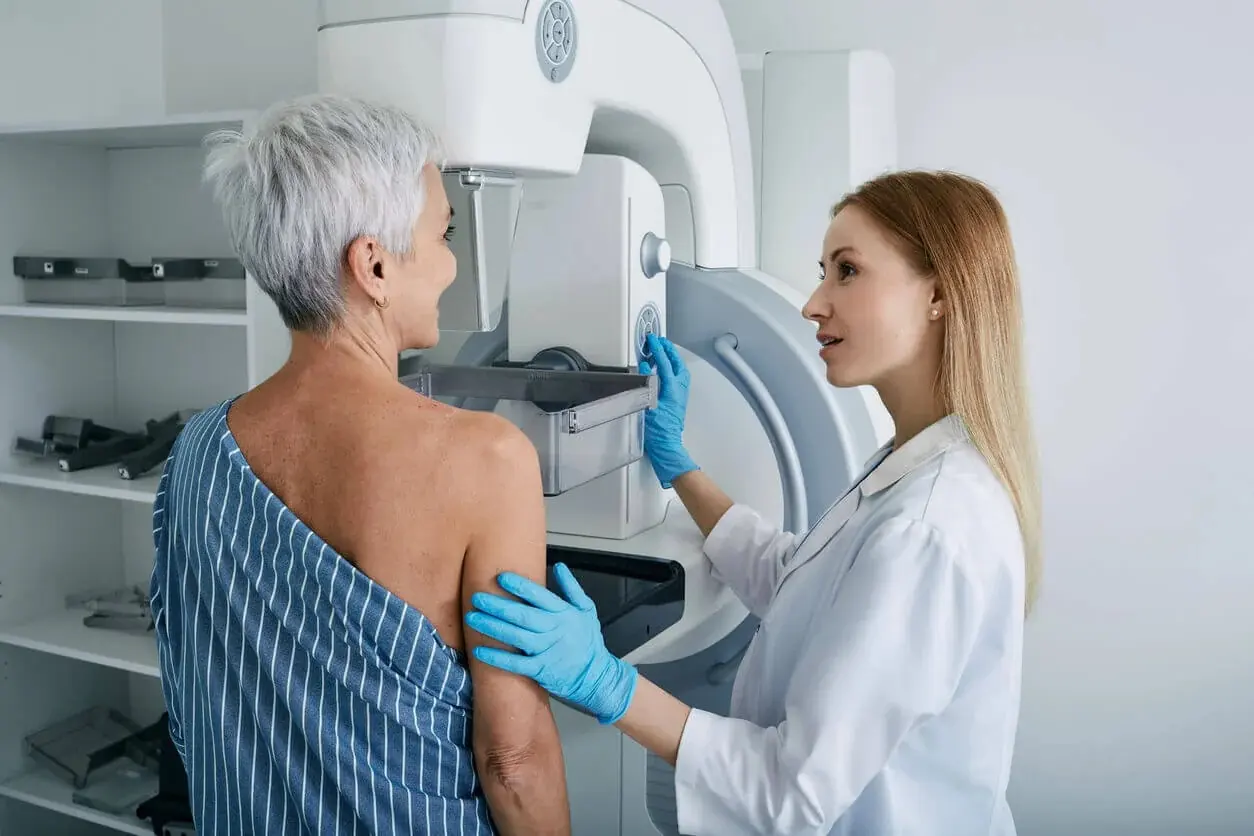A technician positions a patient for a mammogram screening using imaging equipment
