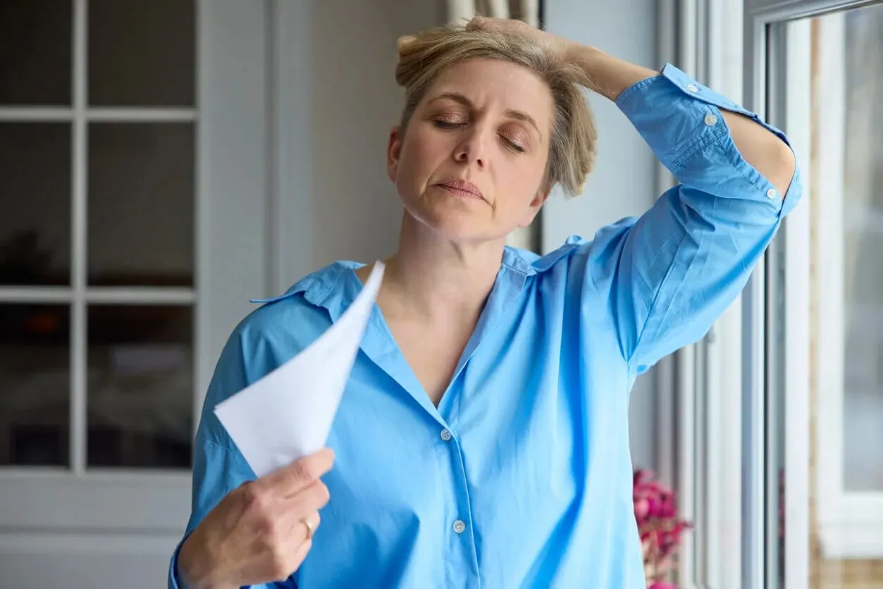 A woman experiences hot flash symptoms of menopause while fanning herself with a piece of paper