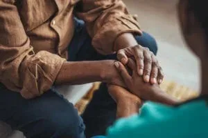 Two people hold hands, offering comfort and support during a mental health conversation