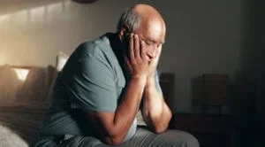 An older adult sits at home showing signs of anxiety and depression, a concern Abundance Health Care helps manage through primary care