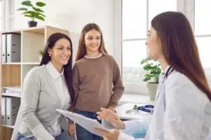 Image of a teenager girl patient with her mother talking with paediatrician doctor in clinic