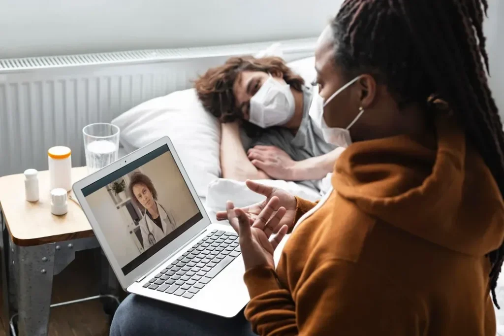 Woman on a telehealth video call with a doctor while caring for a sick friend at home