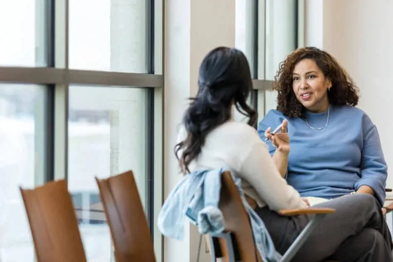 Two women sit near a window having an open conversation during a counseling session