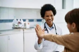 A young girl high-fives her pediatrician alongside her parent during a pediatric appointment at Abundance Health Care